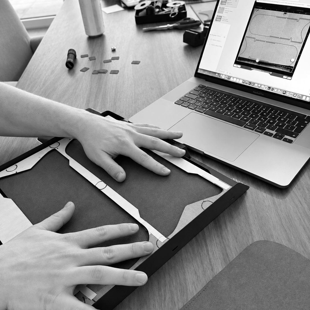 Zwei Hände legen einen Bogen in die Schablone für den Laser, daneben auf dem Laptop die Schnittdatei
