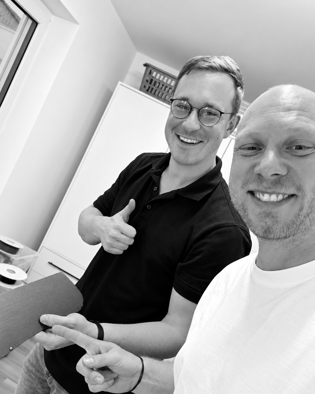 Levin Thome mit Daumen hoch und Sebastian Fischer lachend in der KNIFF-Werkstatt, Levin hält einen zugeschnittenen Bogen LOVR